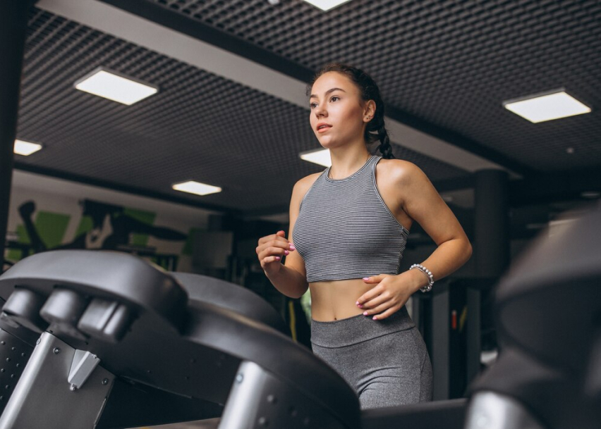 Девушка в спортивном зале бежит по беговой дорожке
